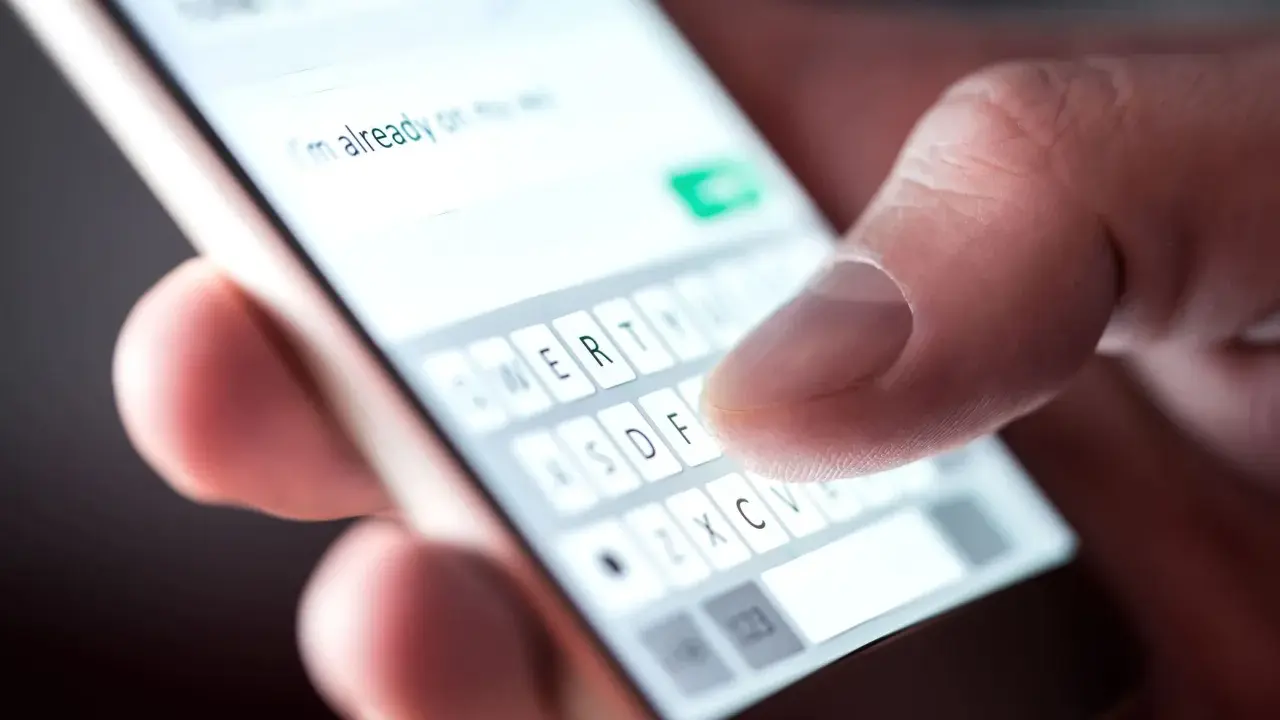 Palec pisze na klawiaturze telefonu: "Już w drodze". Potwierdzenie przybycia na wesele sms.