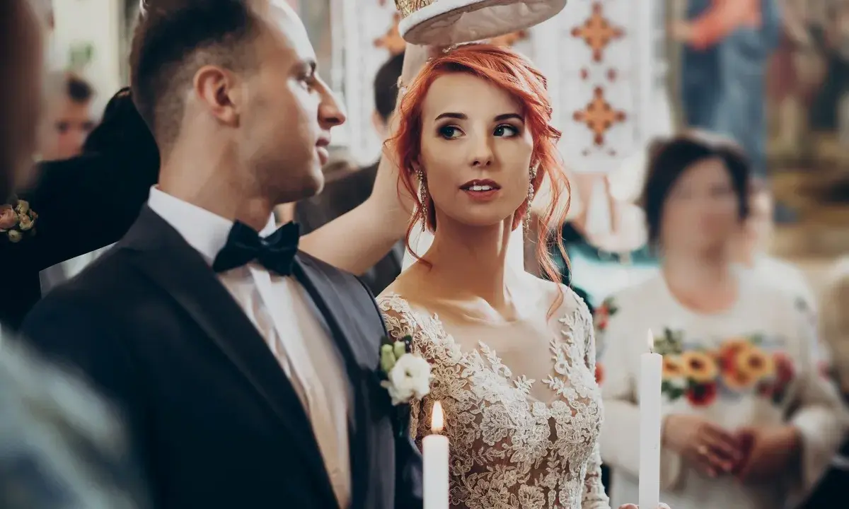 Para młoda podczas ceremonii ślubnej. Panna młoda w koronkowej sukni i pan młody w garniturze, trzymają świece.