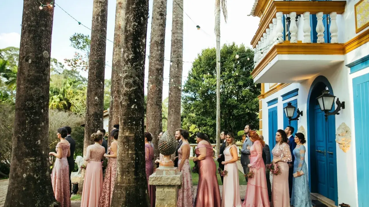 W orszaku panny młodej, panie w różowych sukniach stoją wśród palm, czekając na ceremonię.