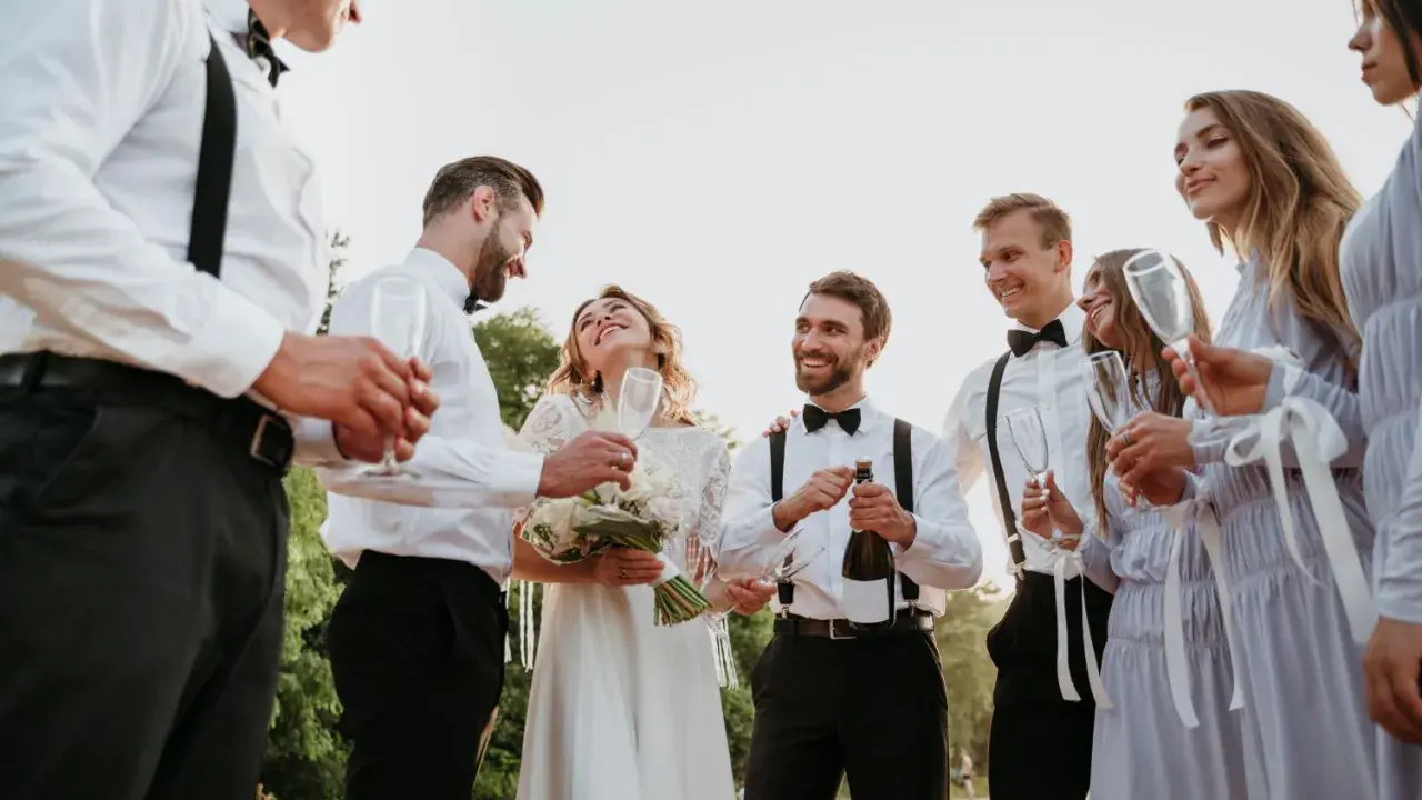 Para młoda świętuje z przyjaciółmi. Czy świadek może być po ślubie? Oczywiście, że tak! Wszyscy są uśmiechnięci i trzymają kieliszki.