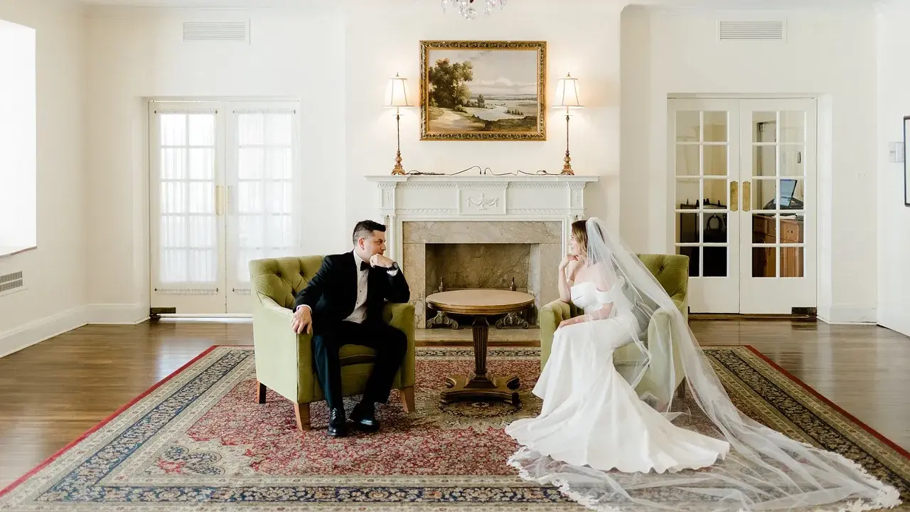 Para młoda siedzi w fotelach, zastanawiając się, ile trwa ślub cywilny. Eleganckie wnętrze z kominkiem i obrazem.