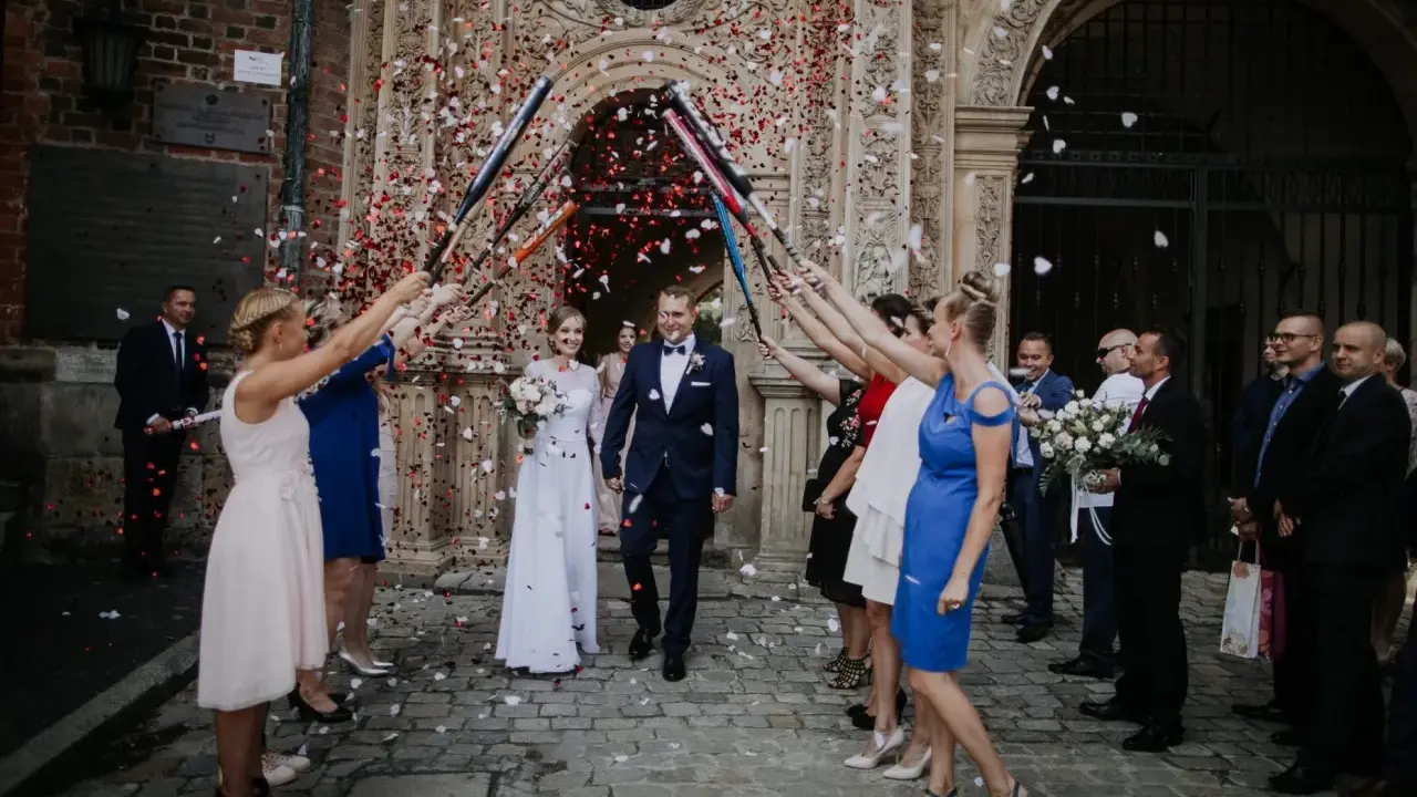 Szczęśliwa para młoda wychodzi z kościoła, obsypana płatkami. Goście z radością świętują wyjście z kościoła ślub.