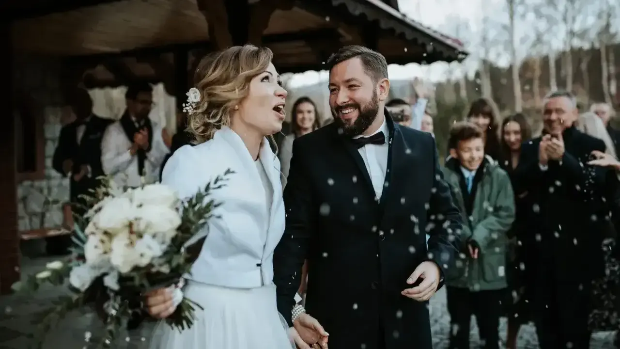 Para młoda wychodzi z kościoła, obsypana konfetti. Mimo że to najgorszy miesiąc na ślub, ich uśmiechy rozświetlają zimny dzień.