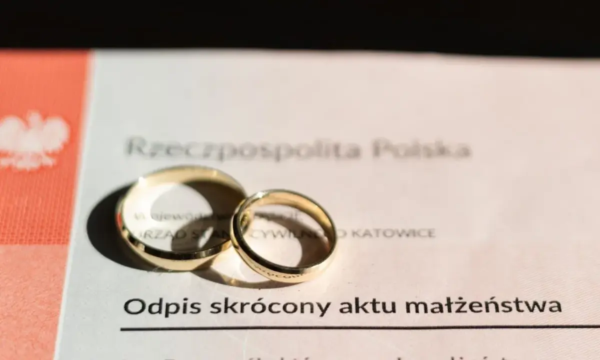 Złote obrączki na odpisie skróconym aktu małżeństwa po ślubie cywilnym. Dokument z Urzędu Stanu Cywilnego w Katowicach.