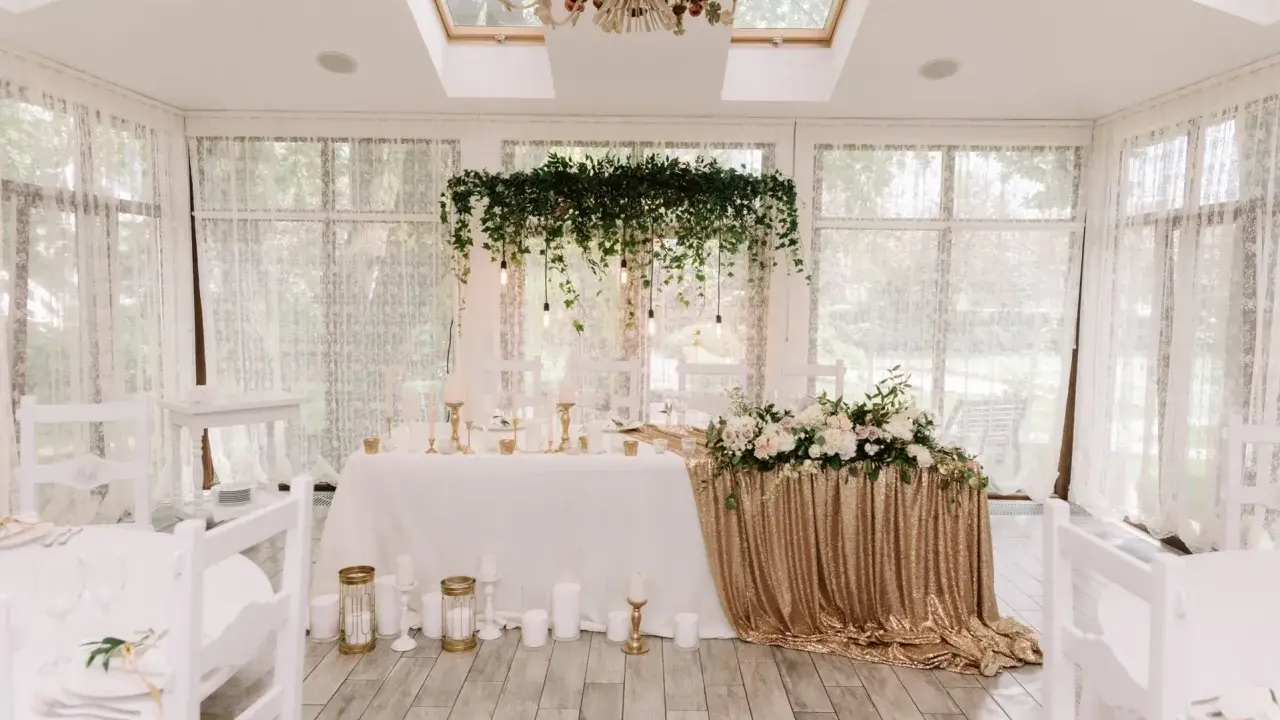 Elegancka sala weselna z białymi krzesłami i stołem pary młodej ozdobionym złotymi cekinami i kwiatami. Wspaniałe kolory na wesele.