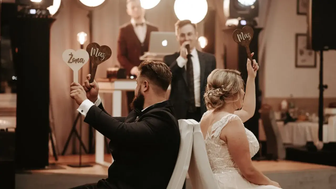 Para zabawy podczas wesela. Ona trzyma tabliczkę "Żona", on "Mąż". Prowadzący zadaje pytania w ramach testu małżeńskiego.