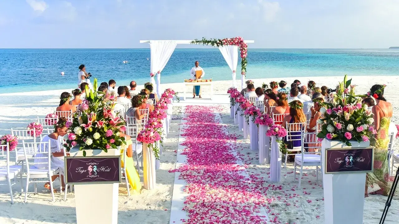 Plażowa ceremonia ślubna z różowymi płatkami kwiatów i błękitnym oceanem w tle. Idealne, nietypowe miejsce na wesele marzeń.