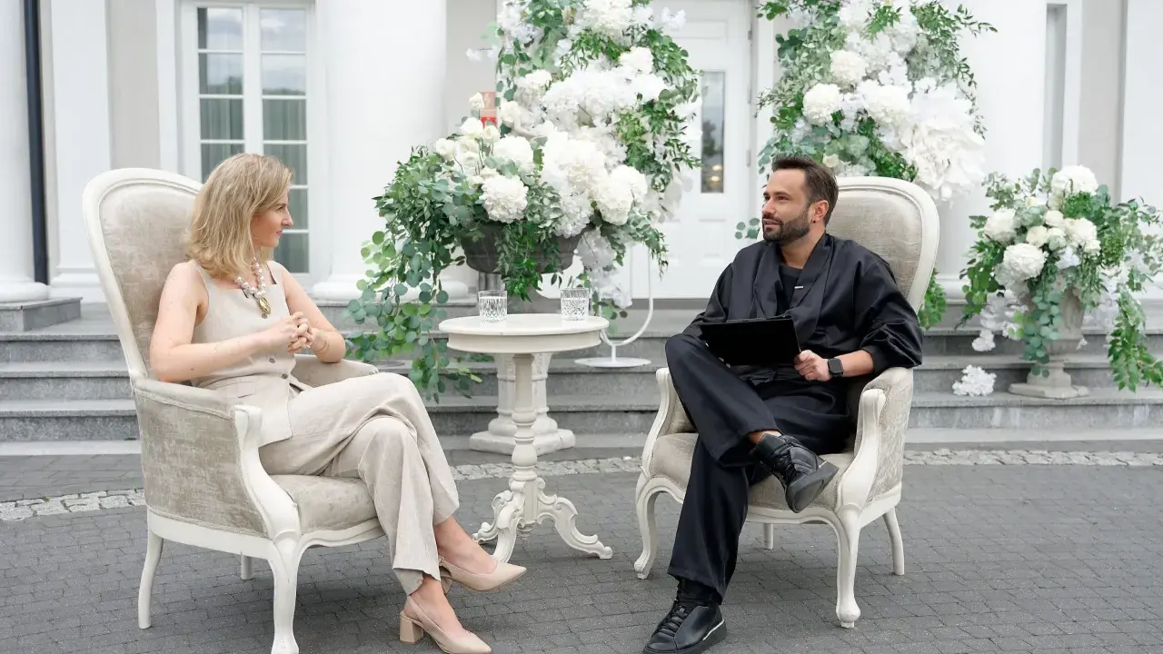 Para, która planuje filmy o weselach, siedzi w eleganckich fotelach wśród białych kwiatów.