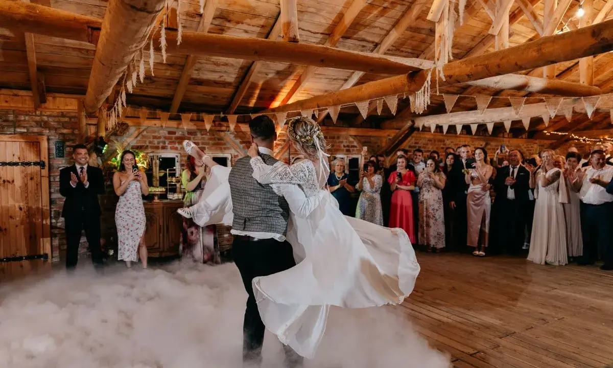 Para młoda tańczy w dymie, tworząc magiczne uroczystości weselne inaczej. Goście obserwują z zachwytem.