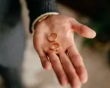 Dłoń mężczyzny trzyma dwie złote obrączki. To symbol tego, kto kupuje obrączki na ślub.