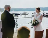 Panna młoda z bukietem w dłoniach patrzy na pana młodego. To ich ślub jednostronny nad jeziorem.