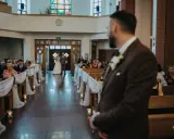 Panna młoda z ojcem idzie do ołtarza. W kościele panują uroczyste warunki ślubu kościelnego, z gośćmi siedzącymi w ławkach.