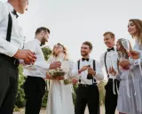 Para młoda świętuje z przyjaciółmi. Czy świadek może być po ślubie? Oczywiście, że tak! Wszyscy są uśmiechnięci i trzymają kieliszki.