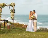 Para Młoda w objęciach, ślub na plaży z widokiem na ocean. Dekoracje z kwiatów i palmy tworzą romantyczną atmosferę.