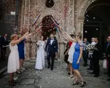 Szczęśliwa para młoda wychodzi z kościoła, obsypana płatkami. Goście z radością świętują wyjście z kościoła ślub.