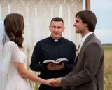 Para młoda trzyma się za ręce, ksiądz błogosławi ich przed ślubem.