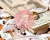 Złote obrączki i stos banknotów, symbolizujące ile daje świadek na wesele. W tle kieliszki szampana.