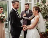 Para młoda trzyma się za ręce podczas ślubu symbolicznego. Pan młody w czarnym garniturze, panna młoda w białej sukni.