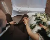 Para młoda trzyma się za ręce, przygotowując się do ślubu konkordatowego. Bukiet ślubny leży obok.