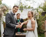 Radość panny młodej podczas ceremonii. Pan młody zakłada jej obrączkę, a urzędniczka patrzy z uśmiechem. Formalności przed ślubem dobiegają końca.