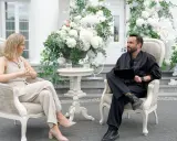 Para, która planuje filmy o weselach, siedzi w eleganckich fotelach wśród białych kwiatów.