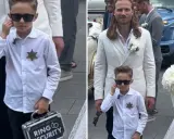 Chłopiec w okularach przeciwsłonecznych, z odznaką i walizką "Ring Security", niesie obrączki do ślubu.
