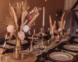 Eleganckie dekoracje na stół weselny z suszonych kwiatów, traw i róż. Złote naczynia i świece tworzą ciepłą atmosferę.