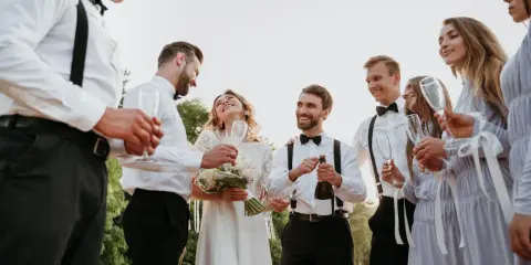 Para młoda świętuje z przyjaciółmi. Czy świadek może być po ślubie? Oczywiście, że tak! Wszyscy są uśmiechnięci i trzymają kieliszki.