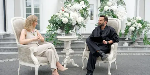 Para, która planuje filmy o weselach, siedzi w eleganckich fotelach wśród białych kwiatów.