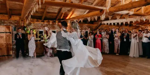 Para młoda tańczy w dymie, tworząc magiczne uroczystości weselne inaczej. Goście obserwują z zachwytem.