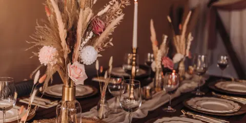 Eleganckie dekoracje na stół weselny z suszonych kwiatów, traw i róż. Złote naczynia i świece tworzą ciepłą atmosferę.