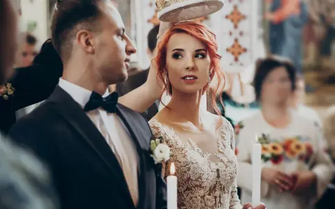 Para młoda podczas ceremonii ślubnej. Panna młoda w koronkowej sukni i pan młody w garniturze, trzymają świece.