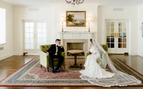Para młoda siedzi w fotelach, zastanawiając się, ile trwa ślub cywilny. Eleganckie wnętrze z kominkiem i obrazem.