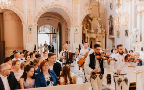 Muzycy w strojach ludowych grają tradycyjne pieśni na ślub w kościele. W tle para młoda wchodzi do świątyni.