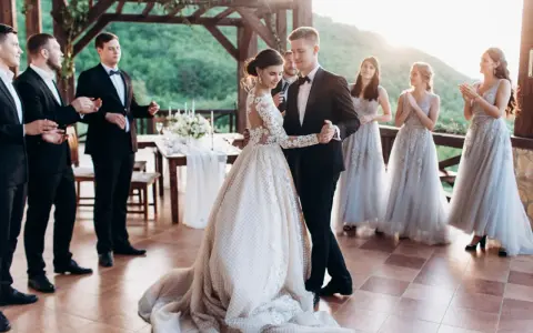 Para Młoda tańczy swój pierwszy taniec. Panna Młoda w pięknej sukni, Pan Młody w eleganckim garniturze. Druhny i świadkowie patrzą z uśmiechem.
