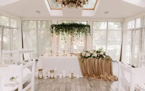 Elegancka sala weselna z białymi krzesłami i stołem pary młodej ozdobionym złotymi cekinami i kwiatami. Wspaniałe kolory na wesele.