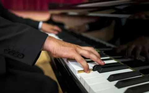 Dłoń muzyka w garniturze gra na fortepianie. Zastanawiasz się, ile bierze organista za ślub?