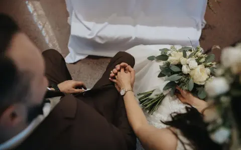 Para młoda trzyma się za ręce, przygotowując się do ślubu konkordatowego. Bukiet ślubny leży obok.