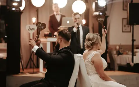Para zabawy podczas wesela. Ona trzyma tabliczkę "Żona", on "Mąż". Prowadzący zadaje pytania w ramach testu małżeńskiego.
