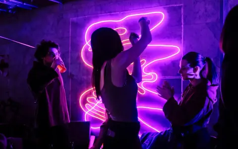 Ludzie tańczą w rytm energicznych piosenek do tańca, w otoczeniu fioletowego neonu.