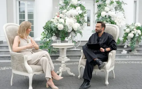 Para, która planuje filmy o weselach, siedzi w eleganckich fotelach wśród białych kwiatów.