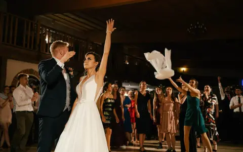 Panna młoda rzuca welonem, tradycyjny moment oczepin. Goście weselni obserwują z ekscytacją.