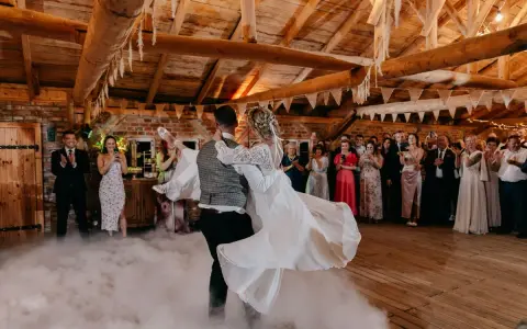 Para młoda tańczy w dymie, tworząc magiczne uroczystości weselne inaczej. Goście obserwują z zachwytem.