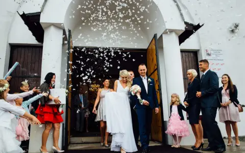 Para młoda wychodzi z kościoła, obsypana płatkami. Radosna geneza wesela, pełna uśmiechów i białych motyli.