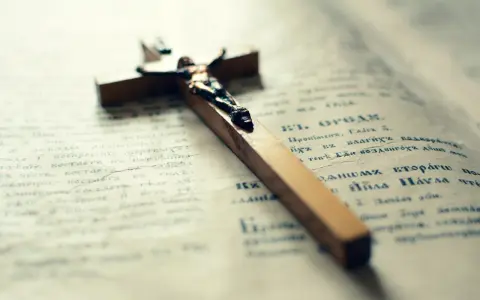 Drewniany krzyż na otwartej księdze. Może symbolizować pytania małżeńskie i duchowe poszukiwania.