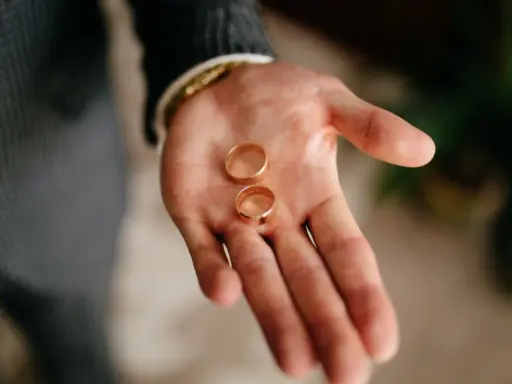Dłoń mężczyzny trzyma dwie złote obrączki. To symbol tego, kto kupuje obrączki na ślub.
