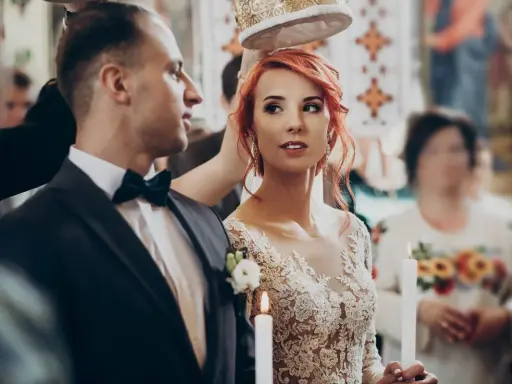 Para młoda podczas ceremonii ślubnej. Panna młoda w koronkowej sukni i pan młody w garniturze, trzymają świece.
