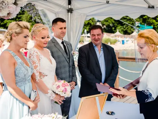 Urzędniczka w przyłbicy wręcza parze młodej dokumenty, symbolizujące ich licencję na ślub.