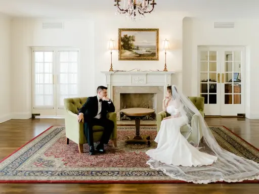 Para młoda siedzi w fotelach, zastanawiając się, ile trwa ślub cywilny. Eleganckie wnętrze z kominkiem i obrazem.