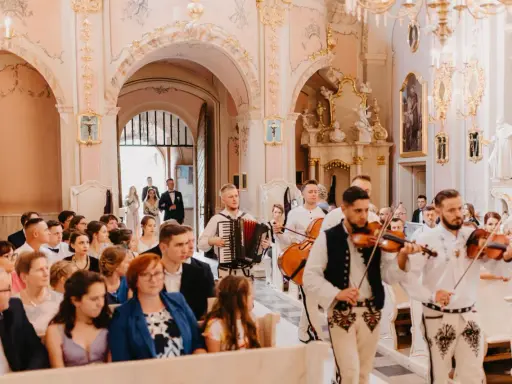 Muzycy w strojach ludowych grają tradycyjne pieśni na ślub w kościele. W tle para młoda wchodzi do świątyni.
